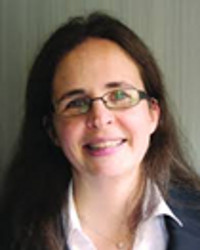 Dr Colette Christiansen, with long dark hair and wearing glasses, smiling at the camera