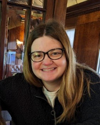 Emma McVan, with long blonde hair and wearing glasses, smiling at the camera