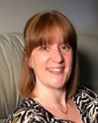 Michelle Coleman, with brown hair, sitting on a sofa and smiling at the camera