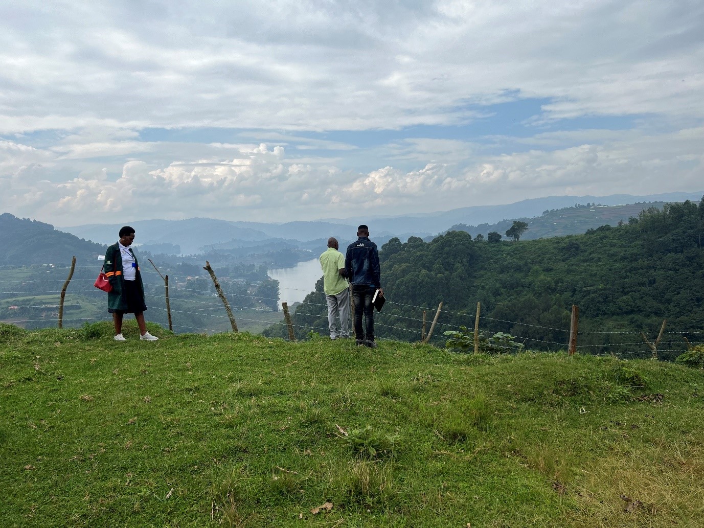 Two men and a woman standing in a field overlooking a lake, forest and mountains in the distance