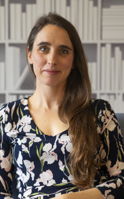 Erica Borgstrom, with long, brown hair, sitting and smiling at the camera, wearing a blue, pink and green floral dress