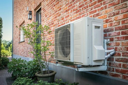 A heatsource pump on a brick wall of a house, with plant pots surrounding it