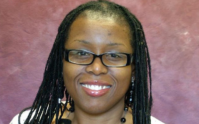 Janice Ansine, with long, dark hair, wearing glasses, smiling at the camera