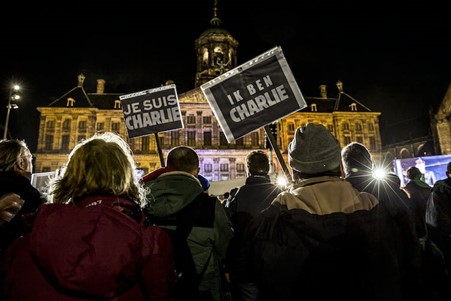 A crowd of demonstrators at night in front of a public building in Amsterdam, holding signs that say Je Suis Charlie and Ik Ben Charlie"