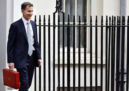 Jeremy Hunt, wearing a dark suit and carrying a red brie case, standing outside a white building with black railings around it