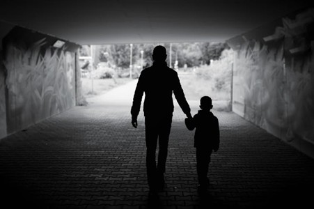 A black and white photo of a man holding a child's hand whilst walking through an underpass