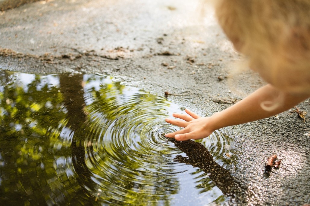 A child putting their finger in a puddle and creating ripples in it