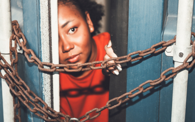 Young girl peering through metal container doors with chains on them