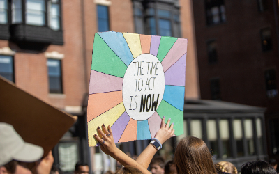 Person holding up a placard with the words 'The time to act is now' written on it