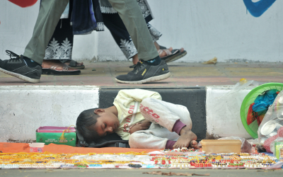 A child lying on a street in Dkaha, Bangladesh, with people walking by
