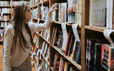 Young girl, with long hair and wearing glasses, browsing books in a library
