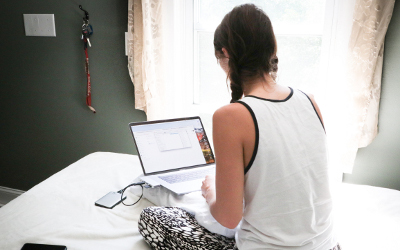 A girl sitting on a bed with a laptop open in front of her