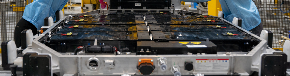 Two men in hard hats working on a car battery