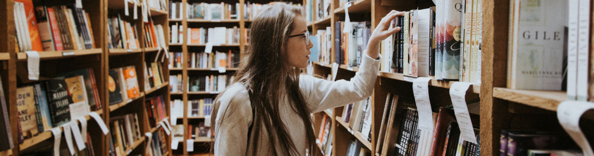 Young girl, with long hair and wearing glasses, in a library, browsing books