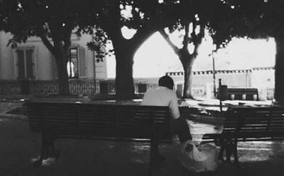A black and white photo of a male refugee sitting on a bench