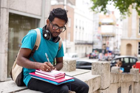 Student outdoors with textbooks and headphones