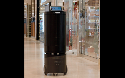 A tall, black, cylindrical-shaped robot in the corridor of a shopping mall