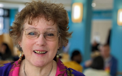 Anne Adams, wearing glasses and a coloured, patterned shirt, smiling and looking at the camera