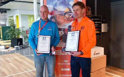 Stijn Baes, on the left, wearing a blue top and jeans, and Bart Rienties on the right, wearing an orange tope and jeans, both standing and holding their certificiates