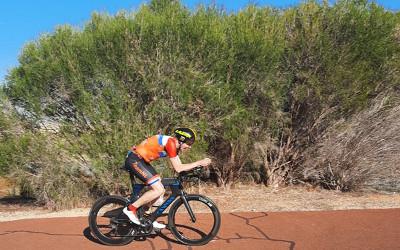 Bart Rienties, wearing an orange top and a bike helmet, riding a bike on a road lined with bushes