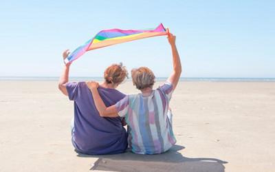 Two people sitting on a beach holding a coloured flag