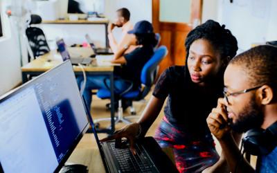 An office with black men and women sitting at tables looking at computer monitors