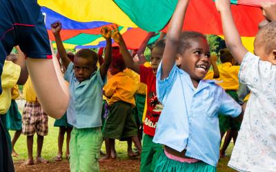 A group of children playing under a colourful parachute