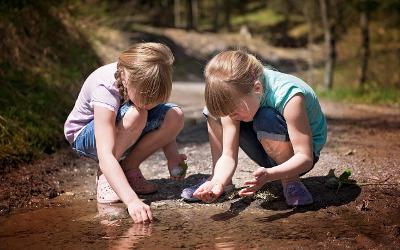 Two young girls crouching down by a stream and looking at things in it