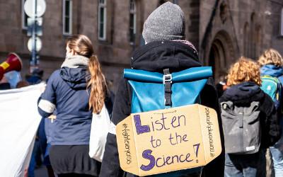 A group of climate change protestors, wearing coats, hats and backpacks, and a sign saying 'Listen to the science'