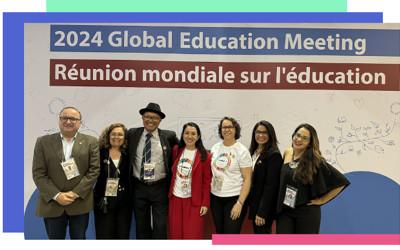 A group of seven men and woman standing underneath a sign saying '2024 Global Education Meeting'