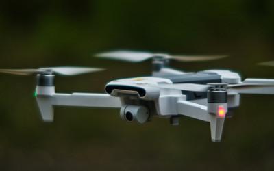 A close up of a drone flying in the air. The drone is white and has four arms with propellors.