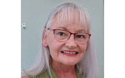 Jaqueline Baxter, with shoulder-length grey hair, wearing glasses and a green top