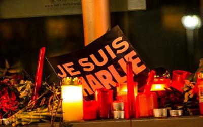 A group of lit candles and a sign with "Je suis Charlie" on it