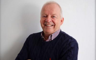 Dr John Morgan, smiling at the camera and wearing a shirt and a dark jumper