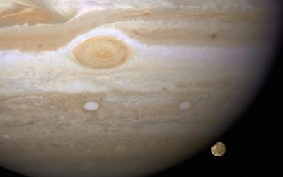 The planet Jupiter with a small icy moon to the bottom right hand side of it in the distance