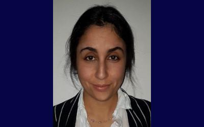 Katherine Staden, with dark hair and wearing a white blouse and black and white striped jacket, looking at the camera