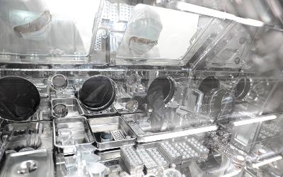 Two scientists wearing protective white clothing and glasses, working with scientific equipment in metal trays. Image credit: Phase 2 Kochi/JAXA