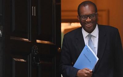 Man in a suit, wearing glasses and holding a document, coming out of a door