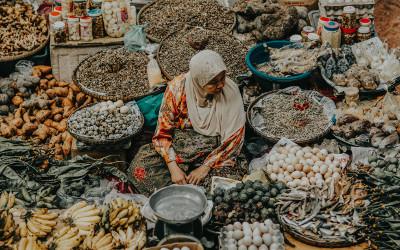 A Malaysian woman, wearing a headscarf, sitting on the ground, surrounded by large bowls of food