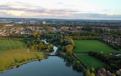 An arial view of Milton Keynes, with a lake and green fields in the foreground and houses and buildings in the background