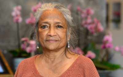 Naila Kabeer, wearing a brown-coloured top and standing in front of an arrange of pink orchids
