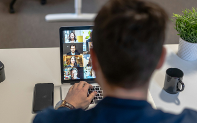 The back view of a person wearing a blue shirt, sitting at a table, looking at a laptop