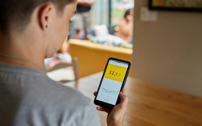 A person looking at data on a mobile phone, with a woman sitting on a sofa in the background