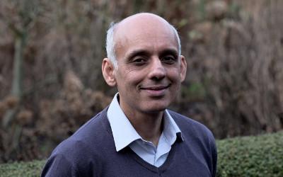 Rajiv Prabhakar, wearing a light-coloured shirt and a blue jumper, standing in front of trees