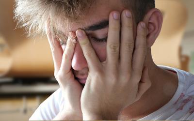 A blond-haired, teenage boy, with his face in his hands, looking sad