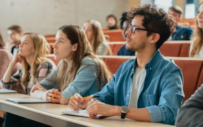 University students in a classroom, listening to a lecture and writing in notebooks