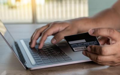 Person's hands, one hand holding a credit card and the other typing on a laptop