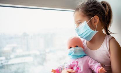 Little girl and doll wearing face masks sitting in window 