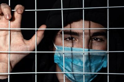 Person wearing facemask behind bars