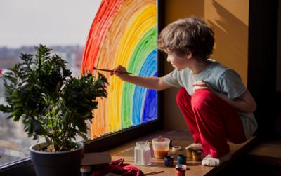 Young boy drawing rainbow on a window